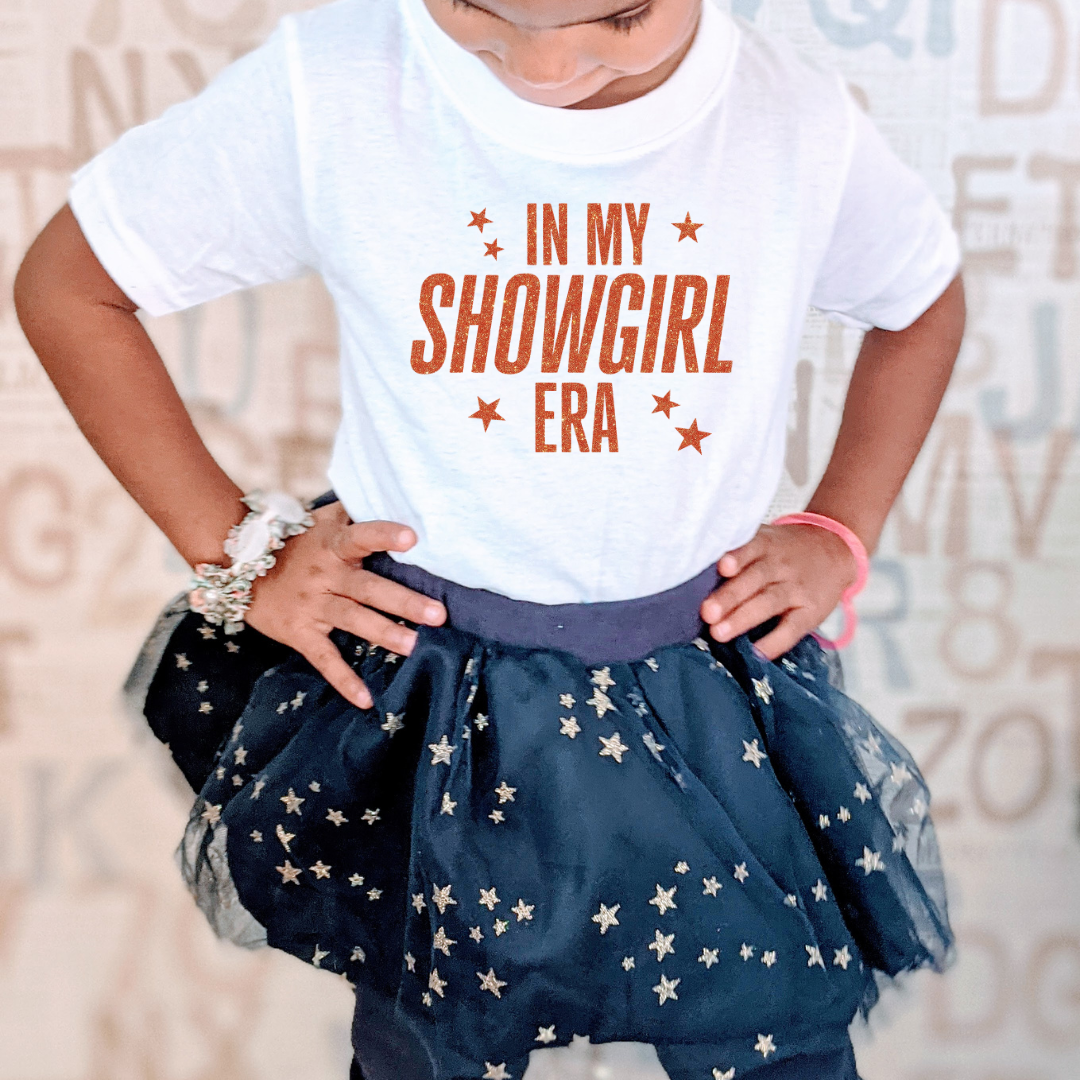 Child wearing a white t-shirt with 'IN MY SHOWGIRL ERA' text and a navy blue star-patterned skirt.