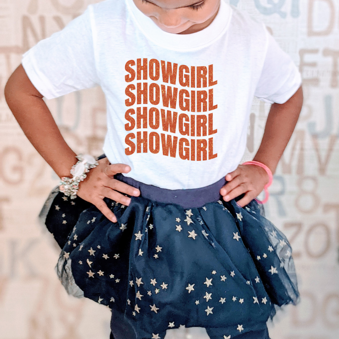 Child wearing a white t-shirt with 'SHOWGIRL' text and a navy blue star-patterned skirt.