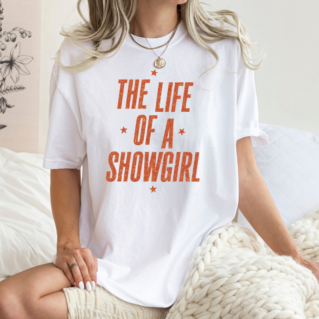 Person wearing a white t-shirt with 'The Life of a Showgirl' text in orange.