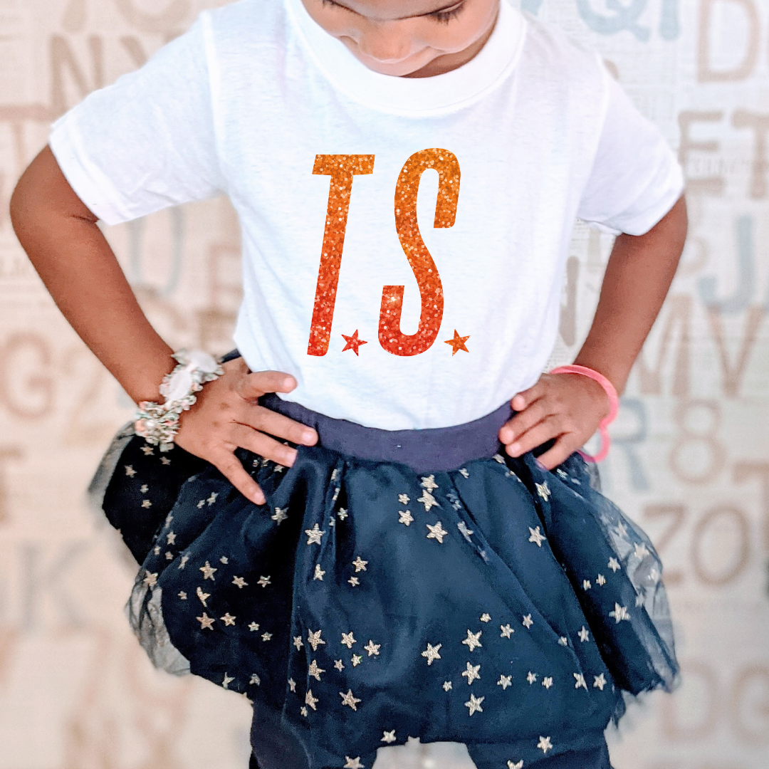 Child wearing a white t-shirt with 'TS' print and a navy blue star-patterned skirt.