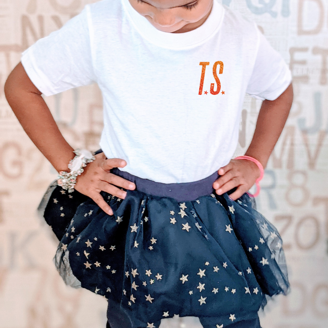 Child wearing a white t-shirt with 'T.S.' and a navy blue tutu with star patterns.
