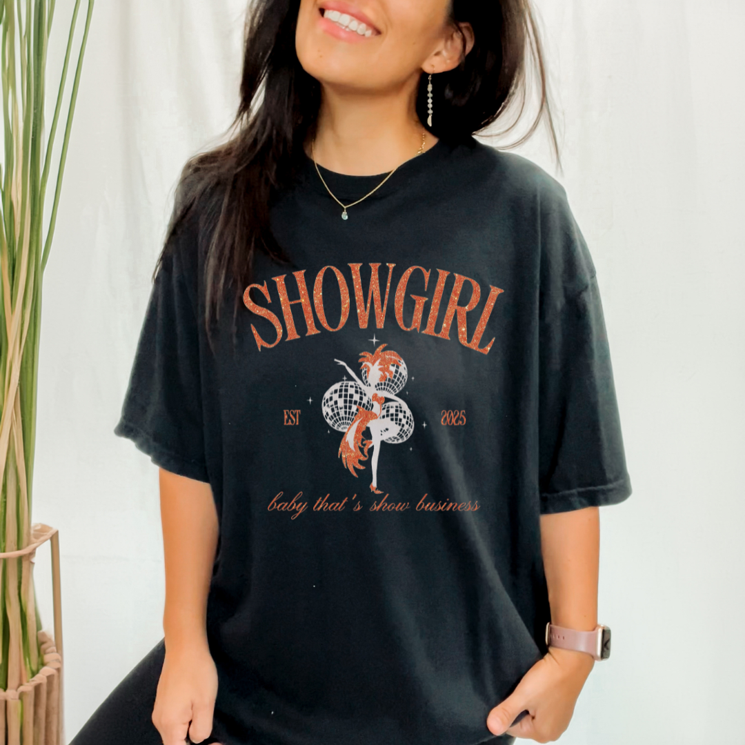 Person wearing a black t-shirt with 'SHOWGIRL' design and text.