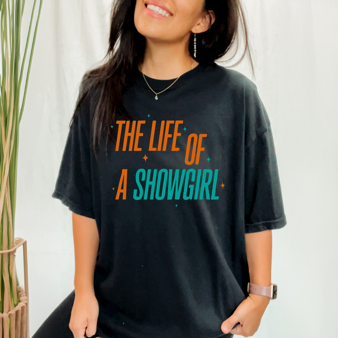 Person wearing a black t-shirt with 'The Life of a Showgirl' text in colorful letters.