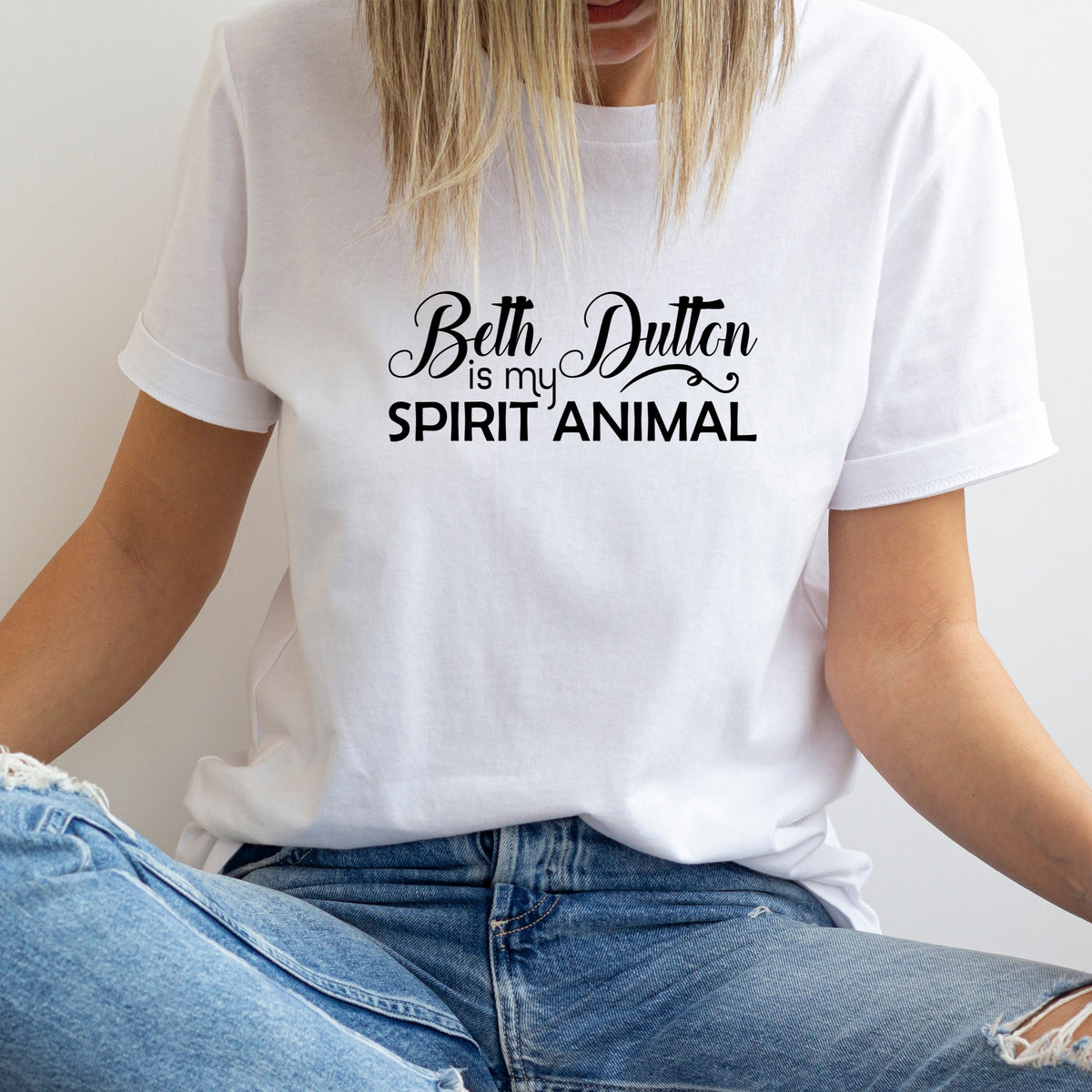 A person wearing a white t-shirt with the text 'Beth Dutton Spirit Animal' printed on the front, paired with blue jeans and white sneakers.