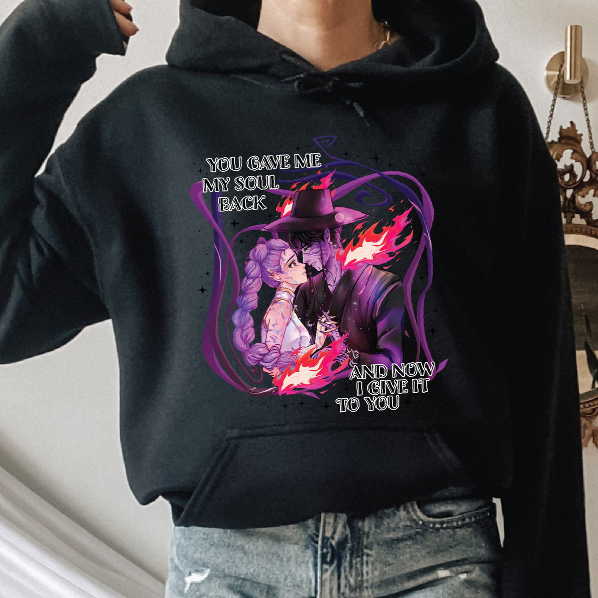 Person wearing a black hoodie with a graphic design and text, standing indoors. Design is graphics from K-pop Demon Hunters
