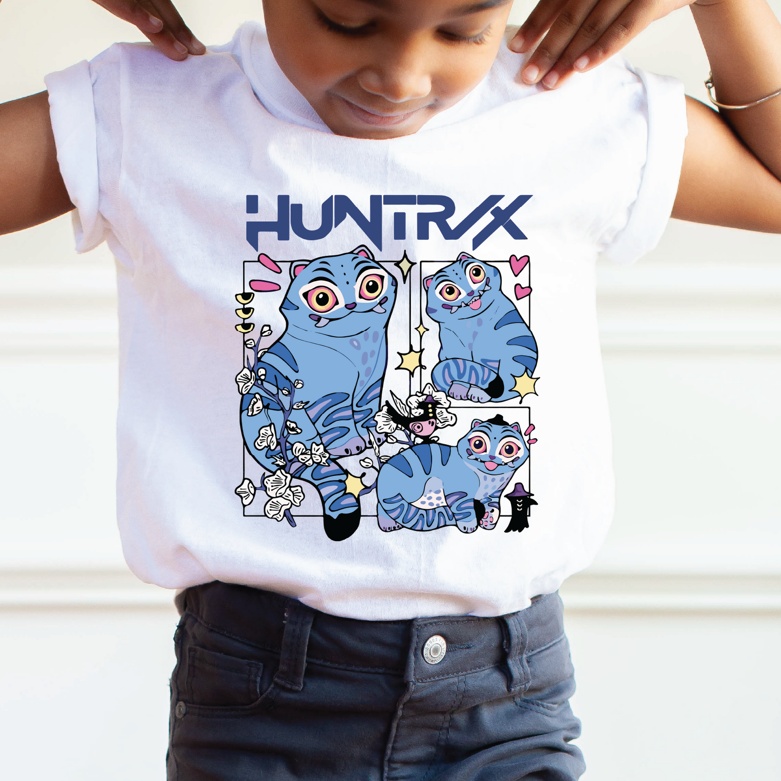 Child wearing a white t-shirt with blue cat illustrations and 'HUNTRAX' text.