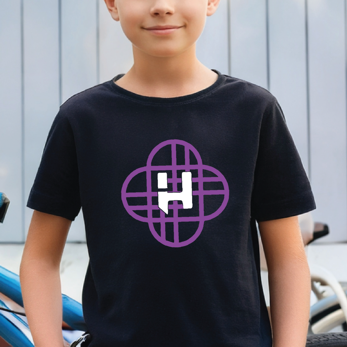 Child wearing a black t-shirt with a purple and white Huntrx logo , standing next to a bicycle.