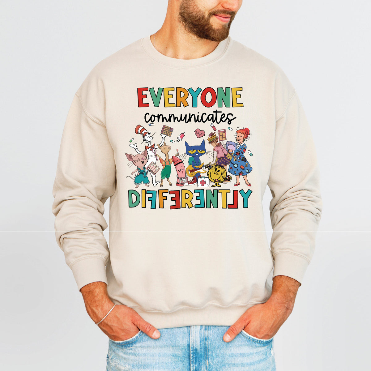 Beige sweatshirt with colorful graphic and text 'Everyone Communicates Differently' worn by a person on a light gray background.