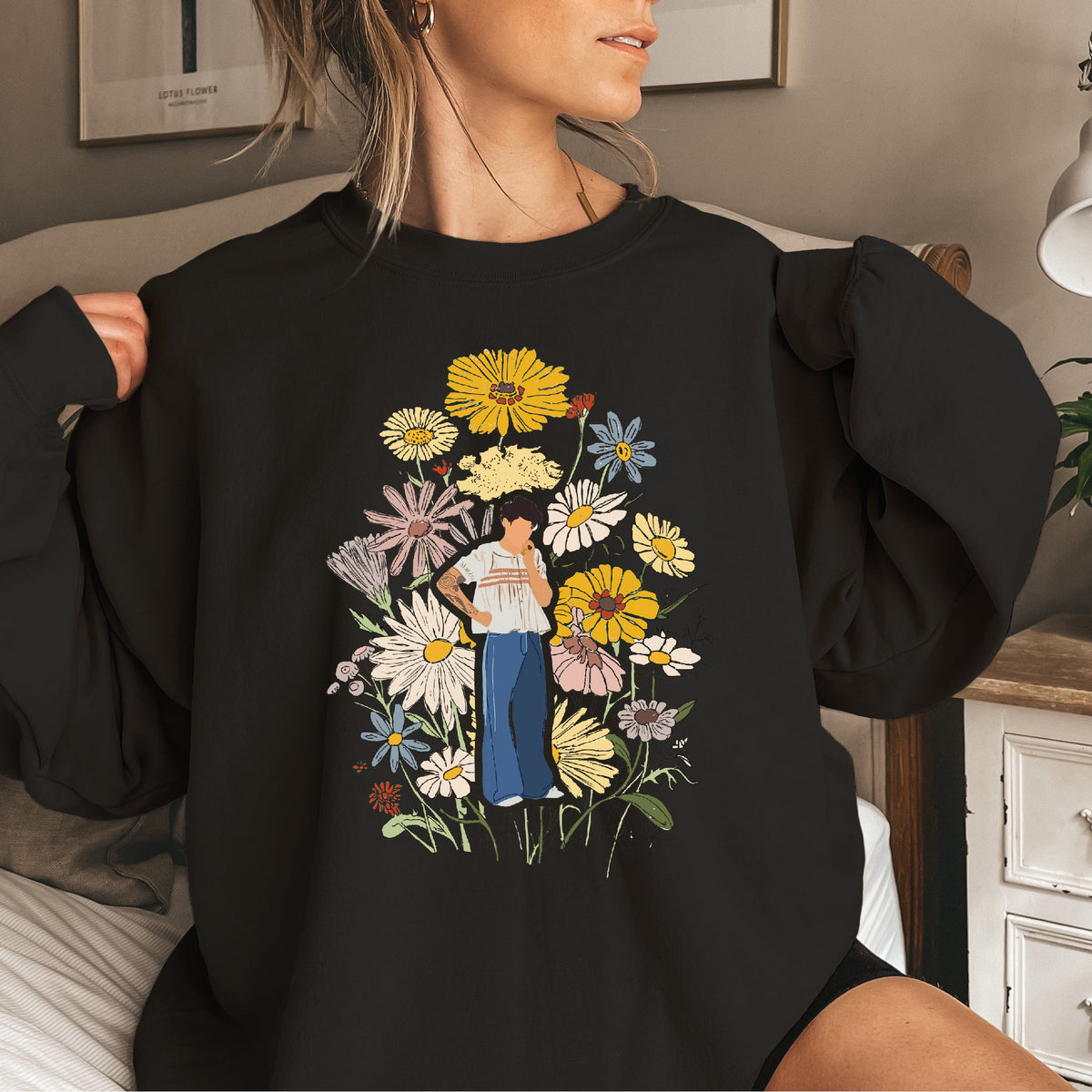 A woman wearing a black oversized sweatshirt with a graphic of a person standing among flowers. Harry's House. Harry Styles.