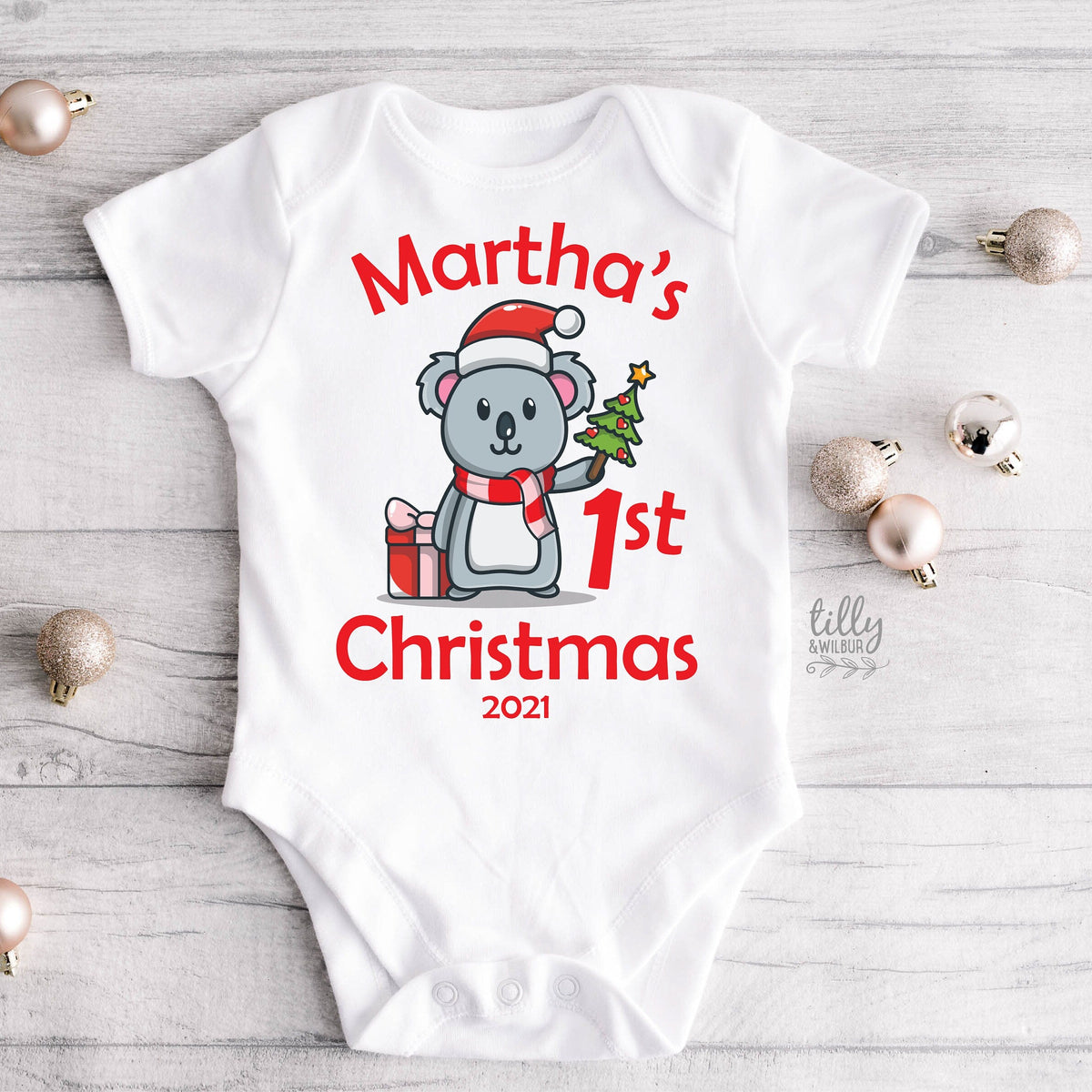 A white baby onesie featuring a cartoon koala holding a Christmas tree and the text 'names 1ST CHRISTMAS and the year'.