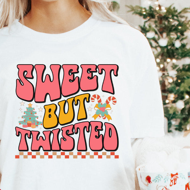 A person holding a mug and wearing a white long-sleeve T-shirt with the text 'SWEET BUT TWISTED' printed on the front, along with the taglines 'Baby, Kids & Adults'.