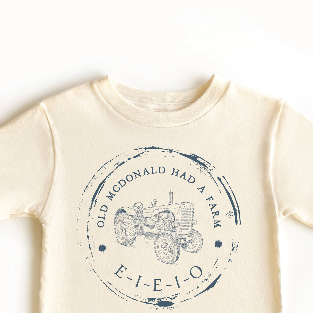 A beige-colored toddler t-shirt with a graphic print of 'Old McDonald Had a Farm' including a tractor illustration and the text 'E-I-E-I-O'.