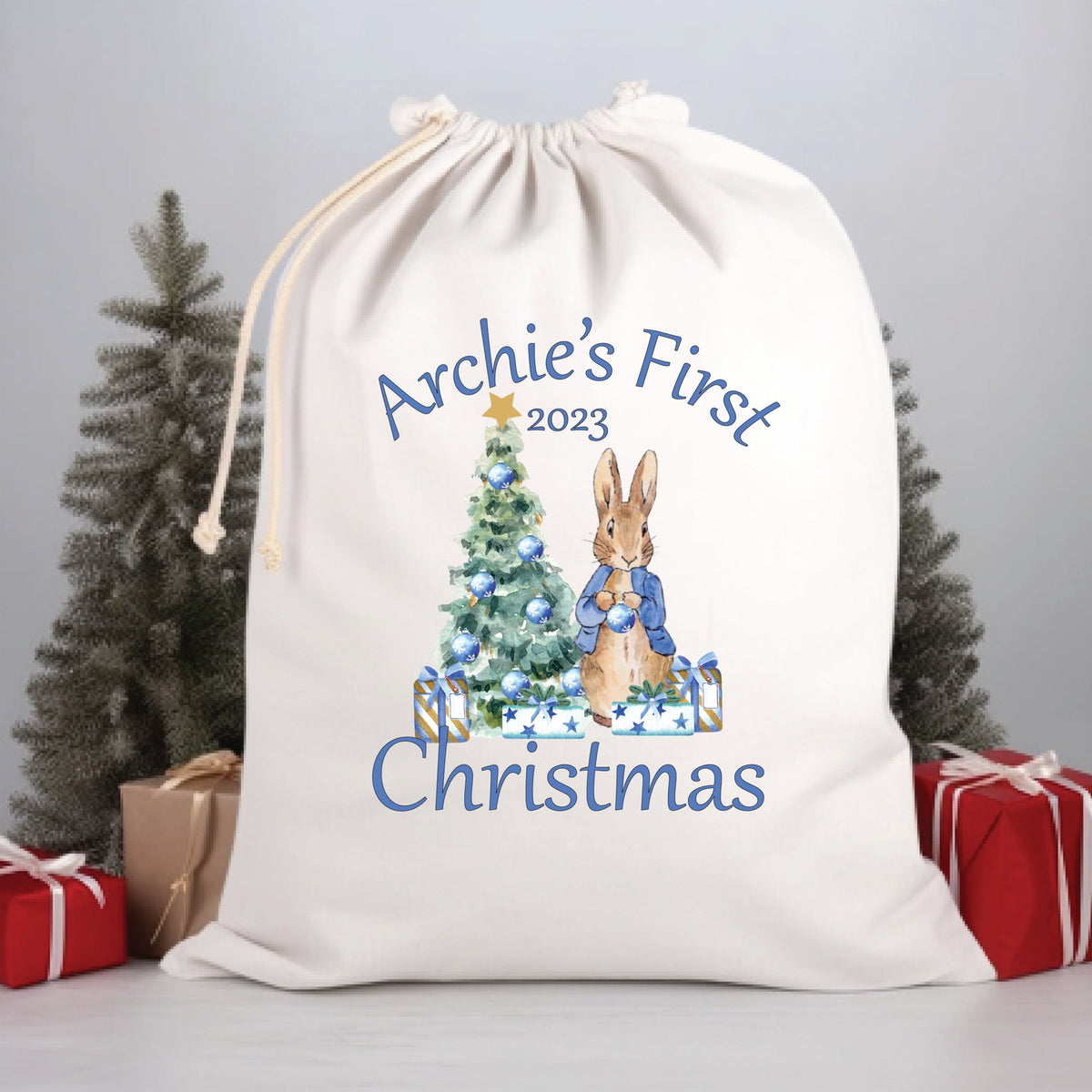 A white Santa sack with the name 'Archie's First Christmas 2023' printed on it, featuring an illustration of Peter Rabbit holding a Christmas tree.