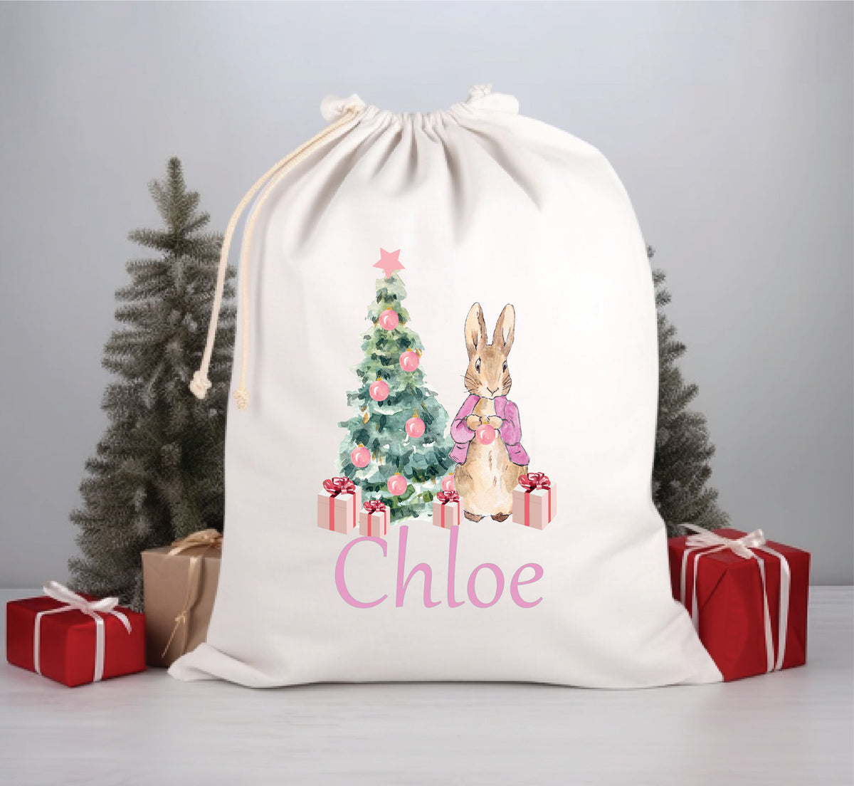 A white Santa sack with a floral pattern, featuring an illustration of a rabbit, a Christmas tree, and presents. The name 'Chloe' is printed in pink on the front.