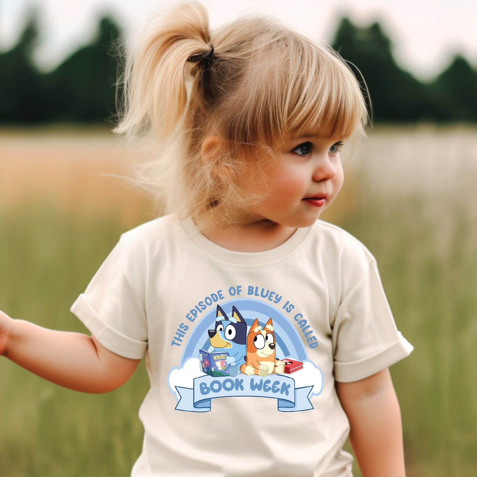 Child wearing a shirt with cartoon characters and text, standing in a field.