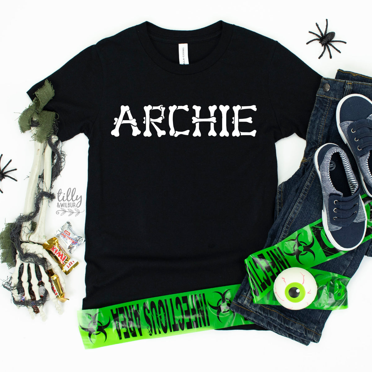 A black T-shirt with 'ARCHIE' written in white bone-like lettering, accompanied by a pair of blue sneakers and green pants, positioned with a skeleton and candy on a white background.