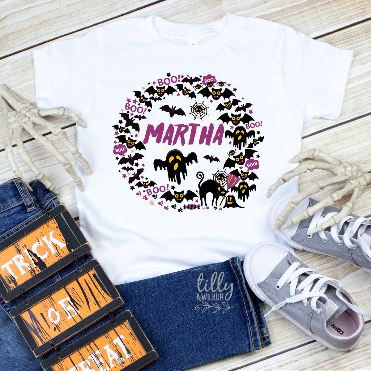 A white t-shirt with a graphic print of bats and pumpkins and the text 'MARIA' and 'TRICK OR TREAT'.