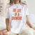 Person wearing a white t-shirt with 'The Life of a Showgirl' text in orange.