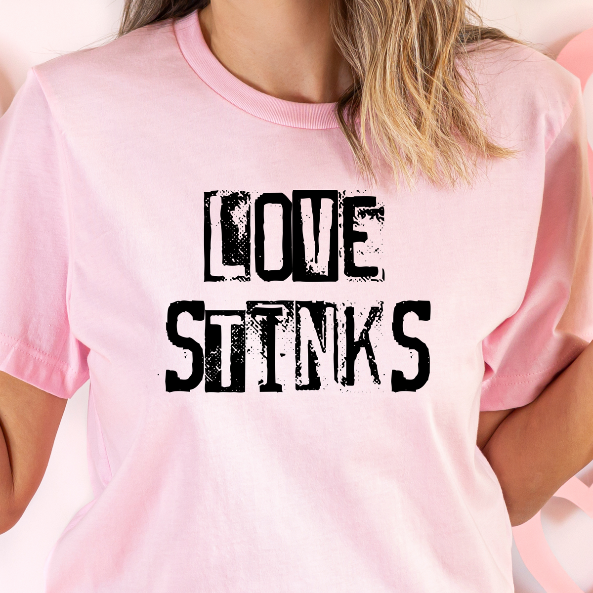 A person wearing a pink t-shirt with the text 'LOVE STINKS' in black capital letters.