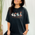 Person wearing a black t-shirt with colorful duck design and text.