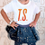 Child wearing a white t-shirt with 'TS' print and a navy blue star-patterned skirt.