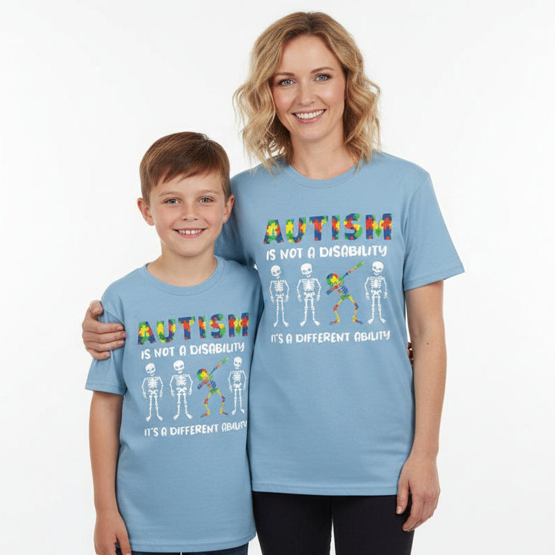 A light blue t-shirt with text and graphics related to autism awareness. The text reads 'AUTISM IS NOT A DISABILITY, IT'S A DIFFERENT ABILITY' accompanied by colorful puzzle piece graphics and skeleton illustrations.
