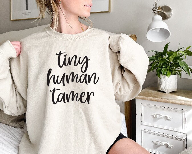 A person wearing a black sweatshirt with the text 'TINY HUMAN TAMER' printed on the front.