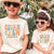 Two children wearing 'Cousin Crew' shirts with personalized names in a tropical setting.