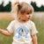 Child wearing a shirt with cartoon characters and text, standing in a field.