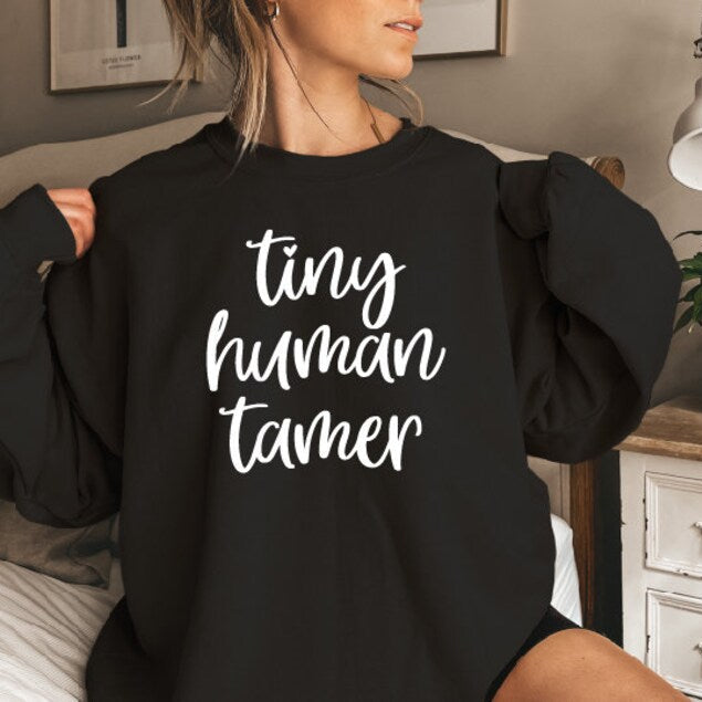 A person wearing a black sweatshirt with the text 'TINY HUMAN TAMER' printed on the front.