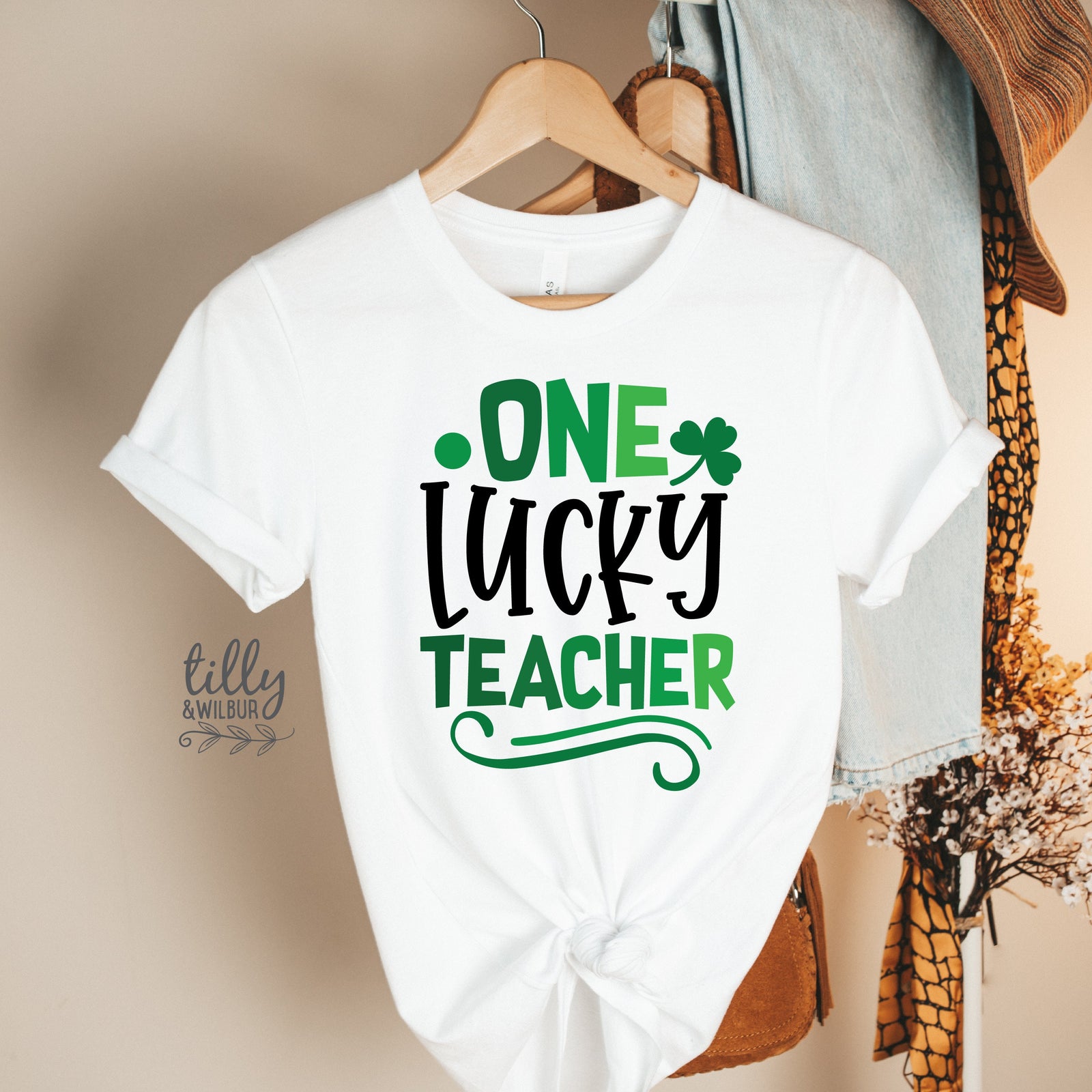 White t-shirt with 'One Lucky Teacher' text in green and black on a white background